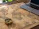 Antique world map with a brass compass on a wooden desk beside a laptop
