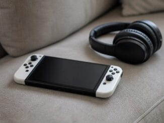 Handheld games console and black headphones lying on a grey sofa cushion