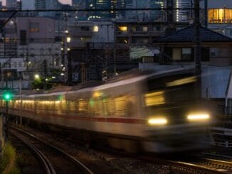 Commuter train speeding through a Japanese city at dusk with light trails