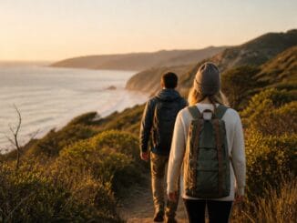 Two hikers walking a coastal trail towards the sea at golden hour