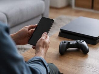 Parent holding a smartphone beside a games console and controller on a coffee table