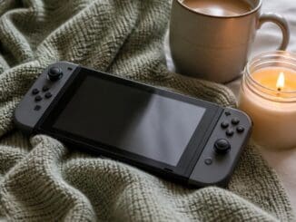 Handheld games console on a knitted blanket next to a mug of coffee and a lit candle