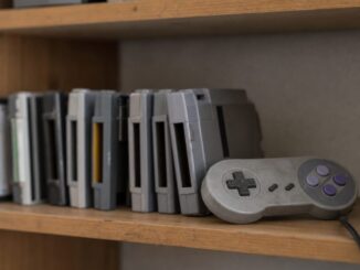 Row of old game cartridges and a grey retro controller on a wooden shelf