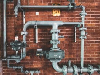 Grey industrial pipes and valves fixed to a brick wall