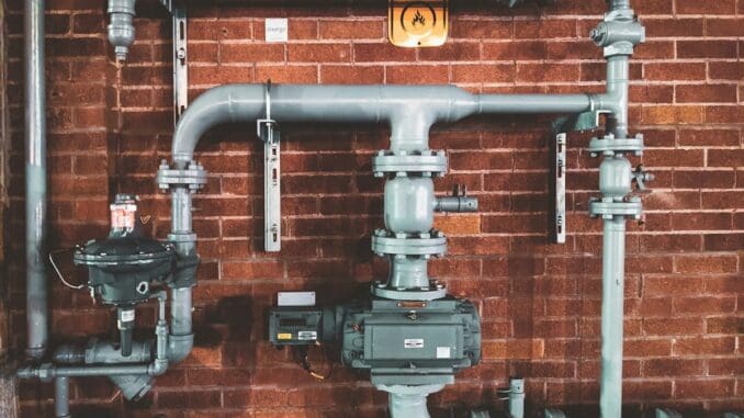 Grey industrial pipes and valves fixed to a brick wall