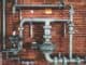 Grey industrial pipes and valves fixed to a brick wall