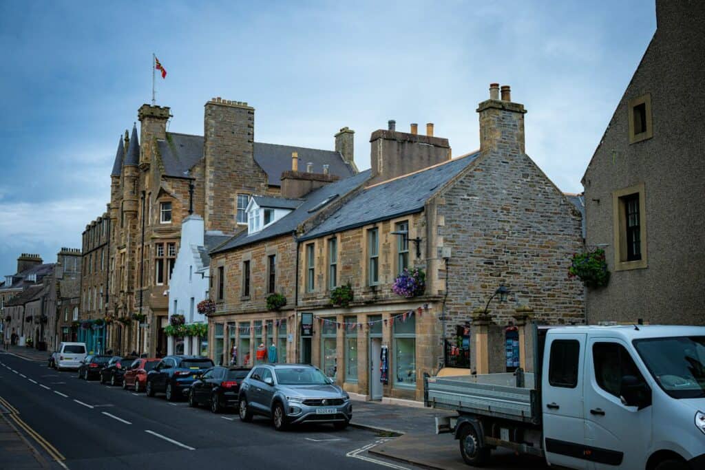 Stone-built town centre street with parked cars and a van