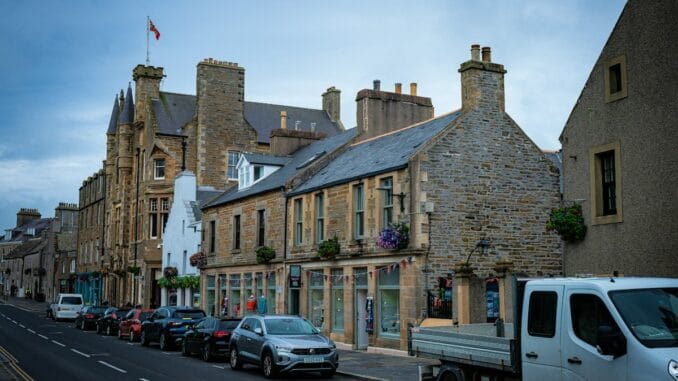 Stone-built town centre street with parked cars and a van