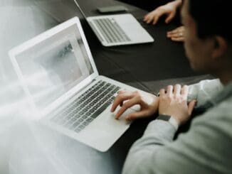 Person typing on a laptop at a table beside a second laptop