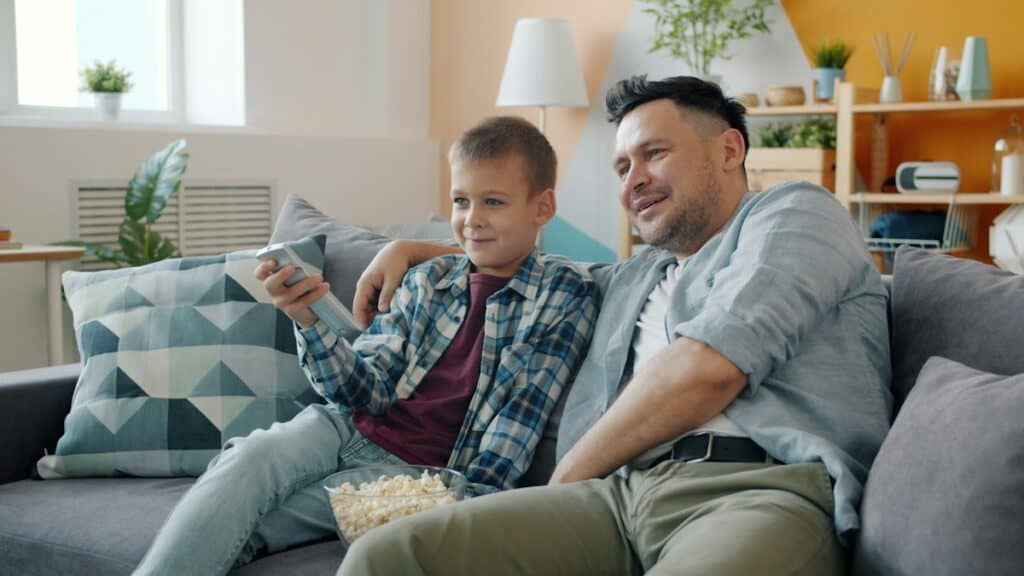 Father and son relaxing on a sofa watching television