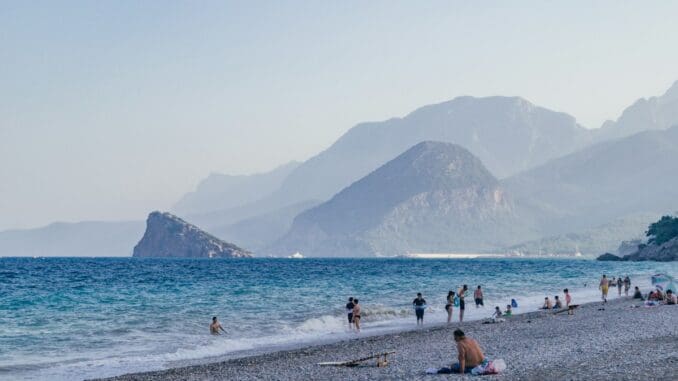 Beach with swimmers below rugged mountains on a sunny coast