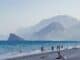 Beach with swimmers below rugged mountains on a sunny coast