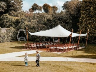 White stretch marquee set up on a garden lawn with chairs beneath it