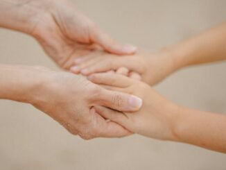 Two pairs of hands gently holding each other against a plain background