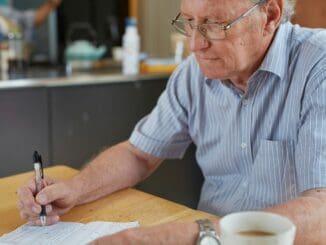 Older man filling in a form at a kitchen table