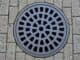 Round metal drain cover set into brick paving