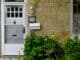 White front door of a stone-built house with plants outside