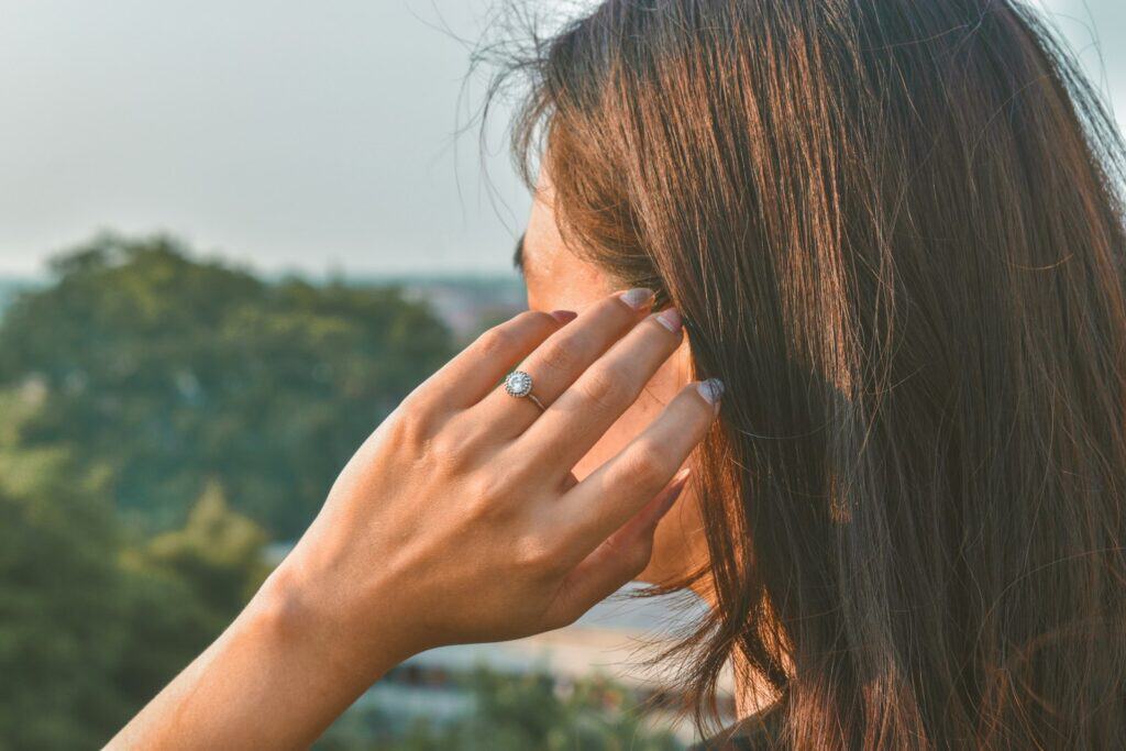Woman with long hair holding her fingers to her ear outdoors
