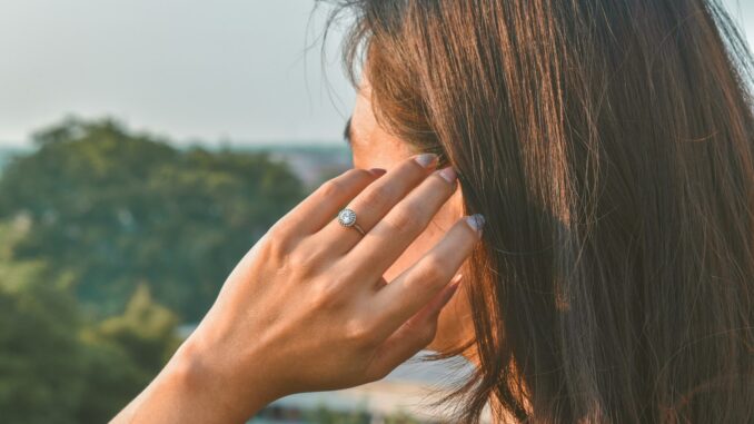 Woman with long hair holding her fingers to her ear outdoors
