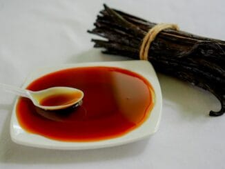 Bundle of dried vanilla pods beside a spoon of dark vanilla extract