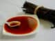 Bundle of dried vanilla pods beside a spoon of dark vanilla extract