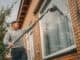 Man cleaning the upstairs windows of a brick house with a long pole