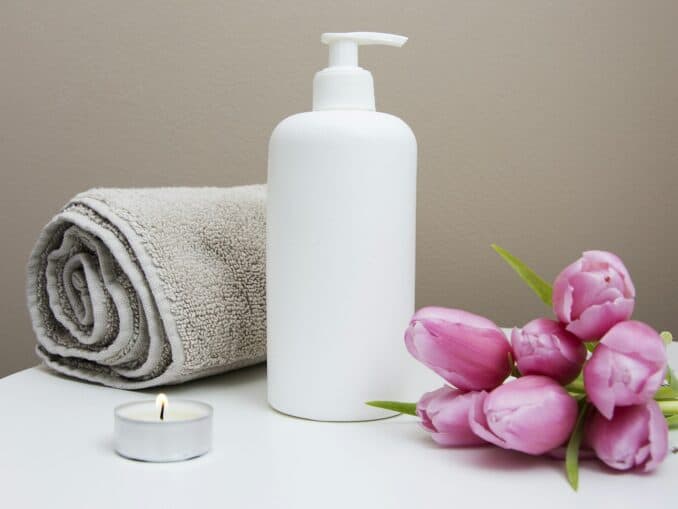 Rolled white towel, pump bottle, tealight and pink tulips on a spa table