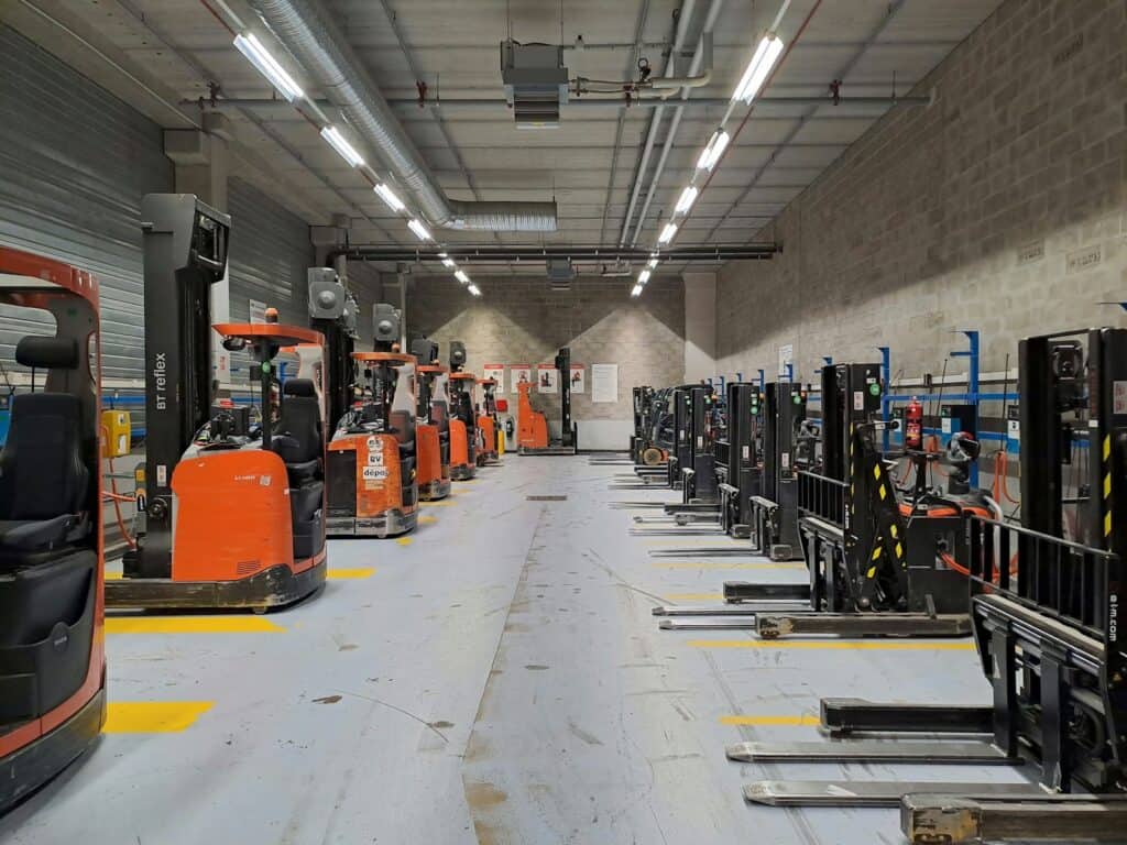 Row of parked forklift trucks in a long, brightly lit warehouse