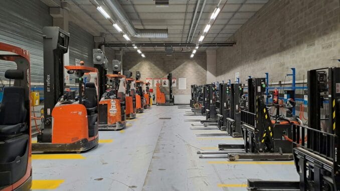 Row of parked forklift trucks in a long, brightly lit warehouse